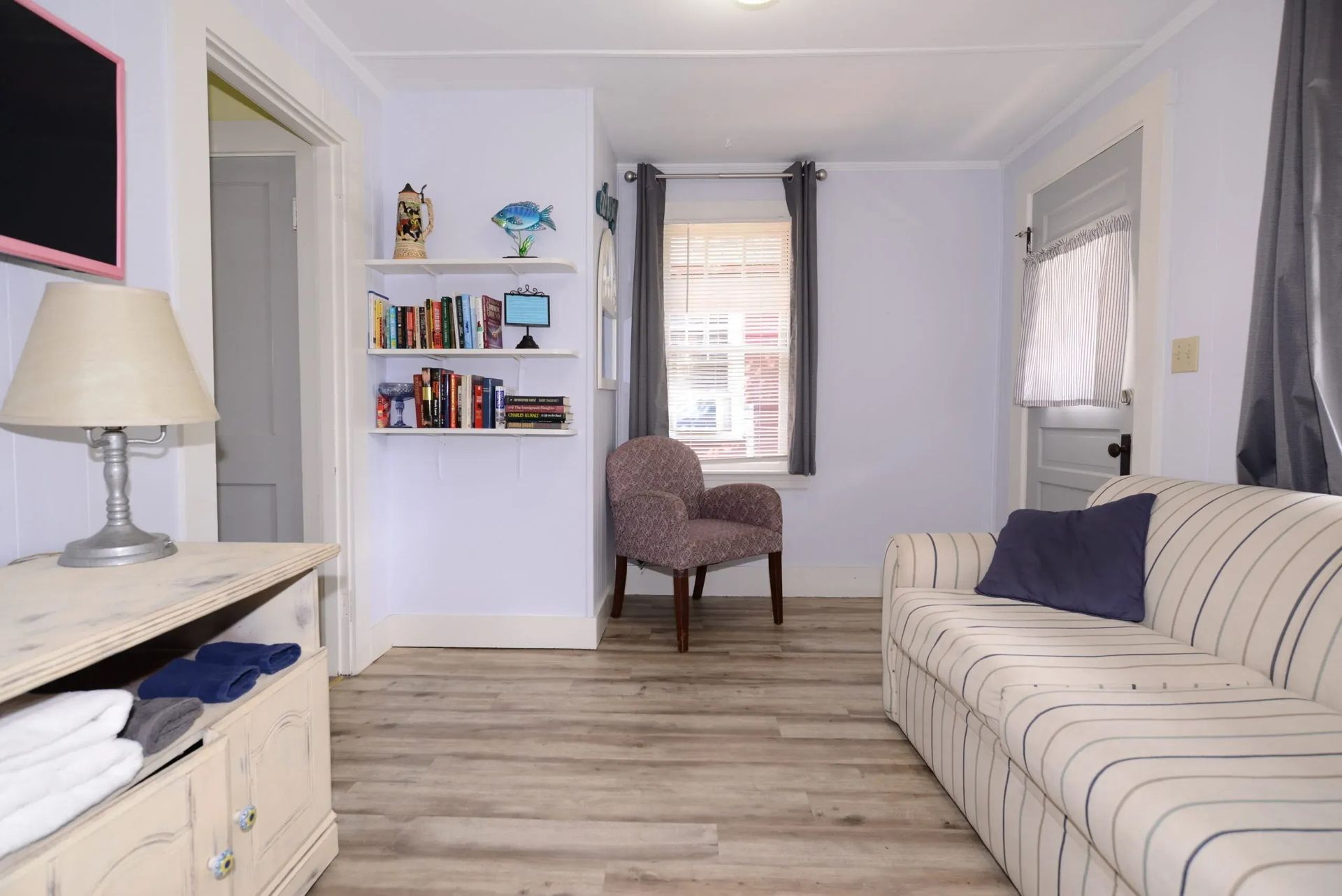 Living room with a sofa, chair, bookshelves, window, and wood-look flooring.