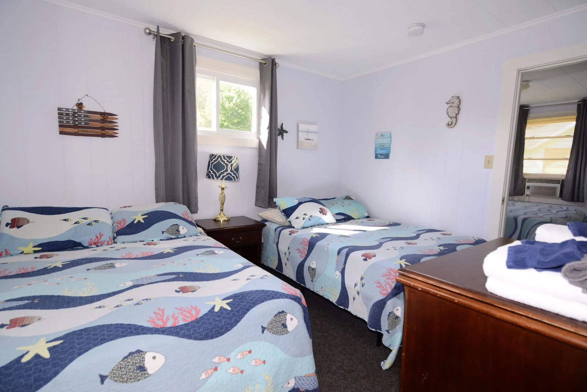 Bedroom with two twin beds, ocean-themed bedding, a nightstand with a lamp, and a dresser.