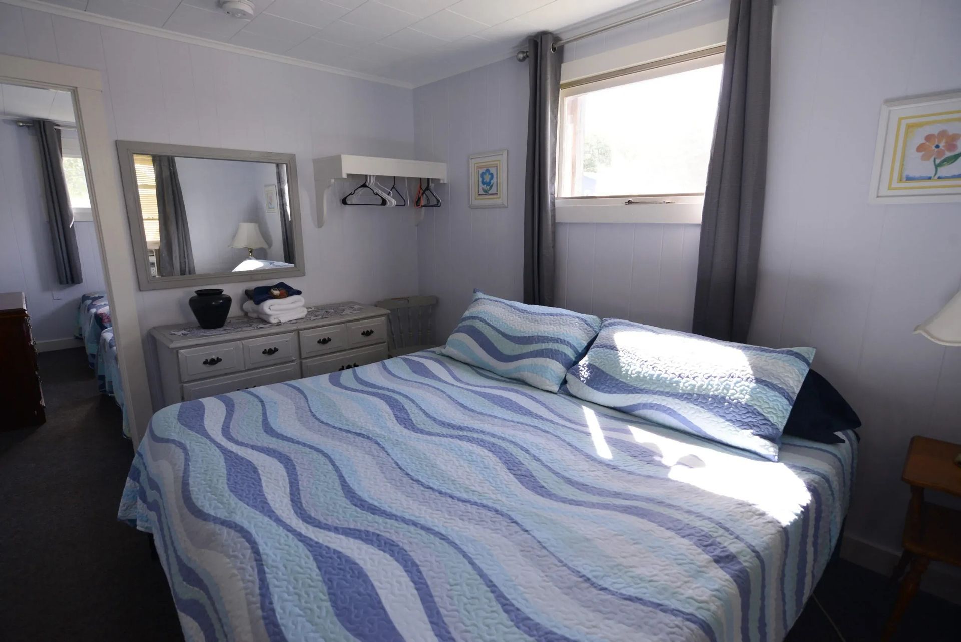 Bedroom with a bed, dresser, mirror, window, and grey curtains. 