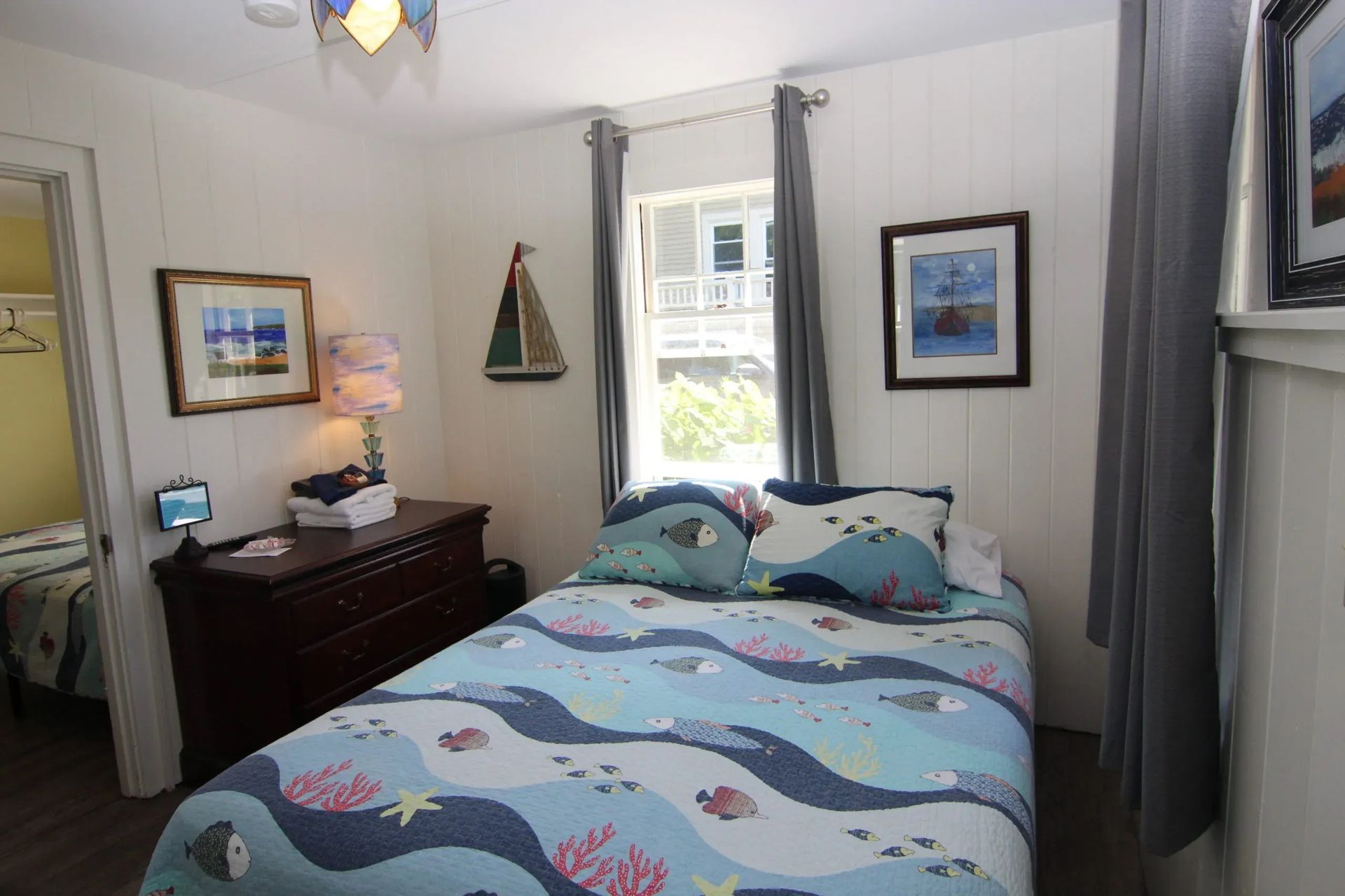 Cozy bedroom with a bed, nautical decor, artwork, and a window with gray curtains.