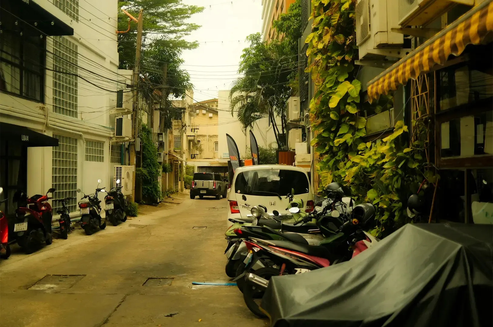 A calm, peaceful residential street in Bangkok lined with buildings on either side with park vehicle