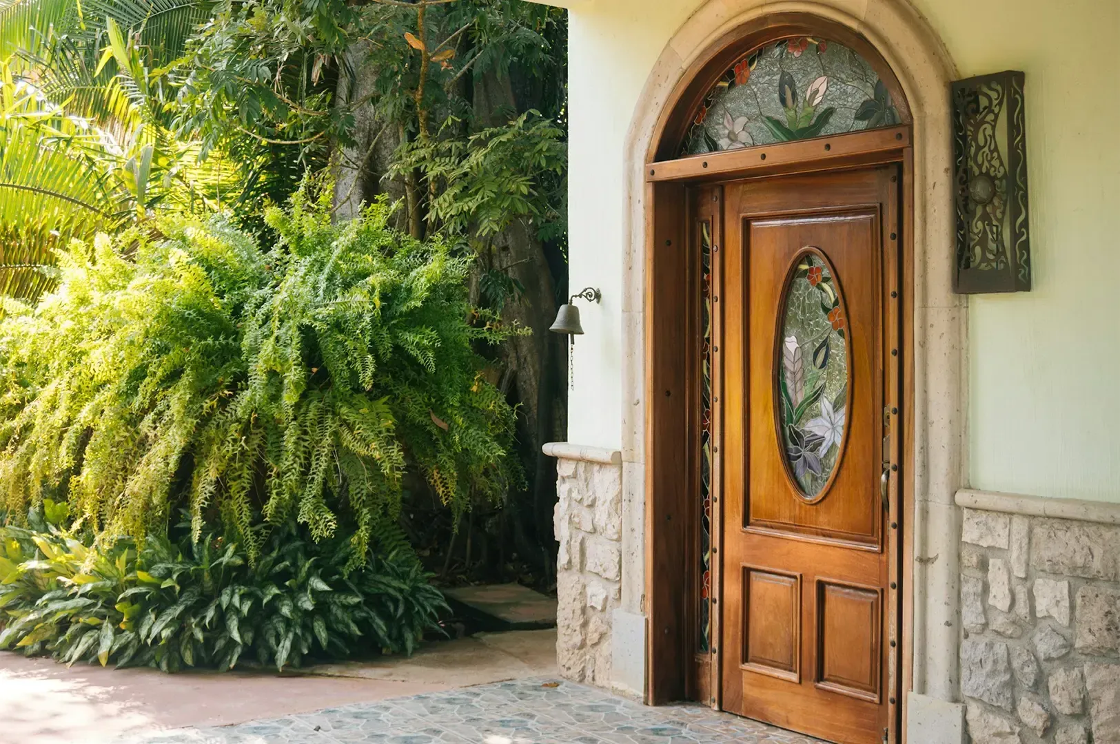 A front door with intricate carved designs and stone brick wall on either side with greenery growing
