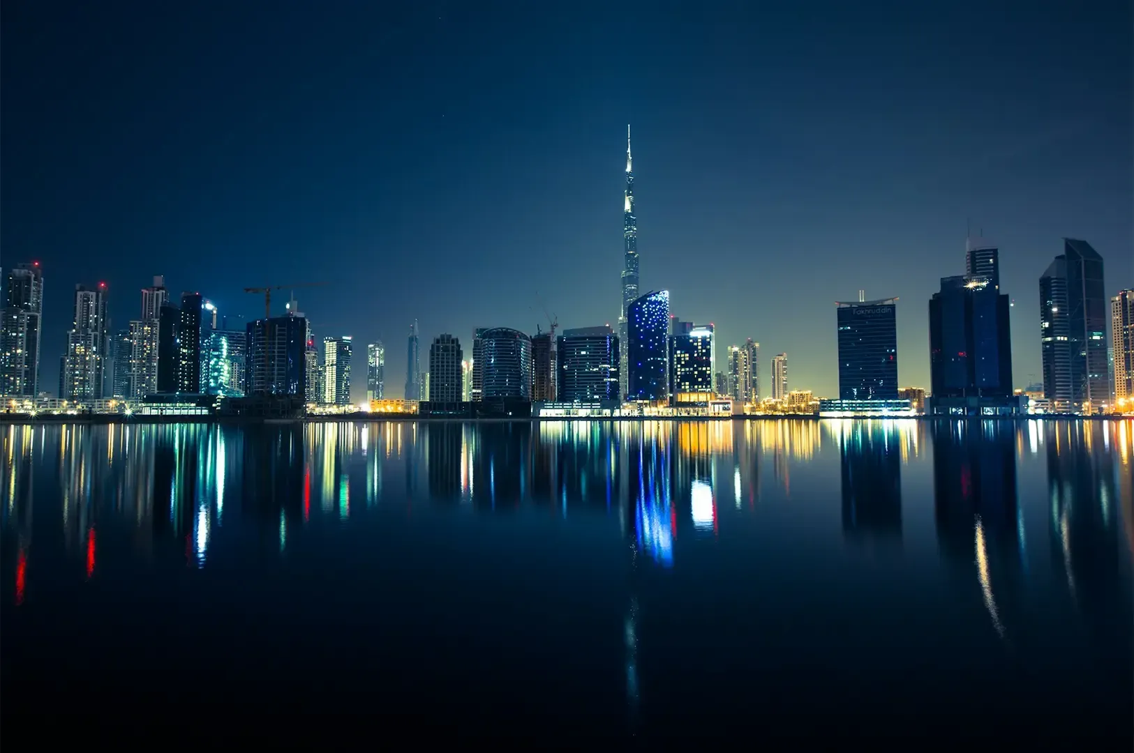 Dubai city skyline with the high rise buildings and their bright multicolored lights reflecting on w