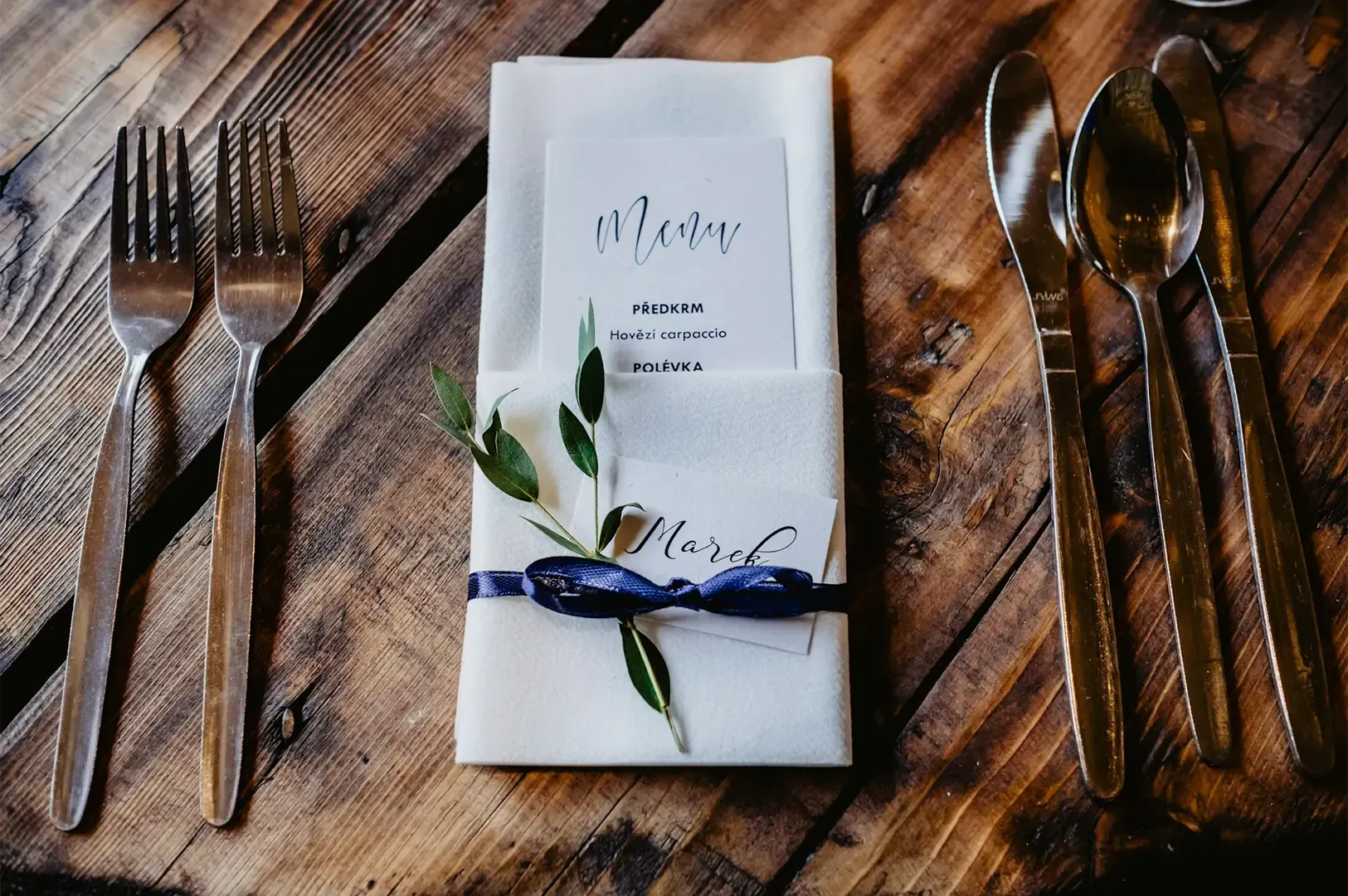 A fine dining menu placed in a neat white napkin designed with ribbons and leaves with cutlery arran
