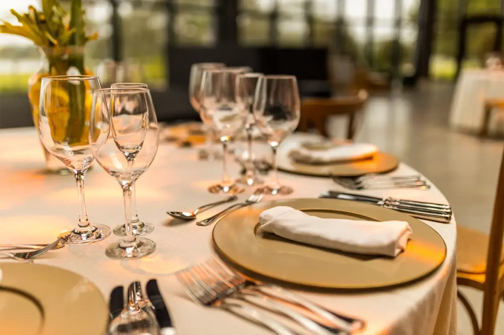 A close up shot of neatly arranged utensils and glasses on a dining table decorated with a vase and 