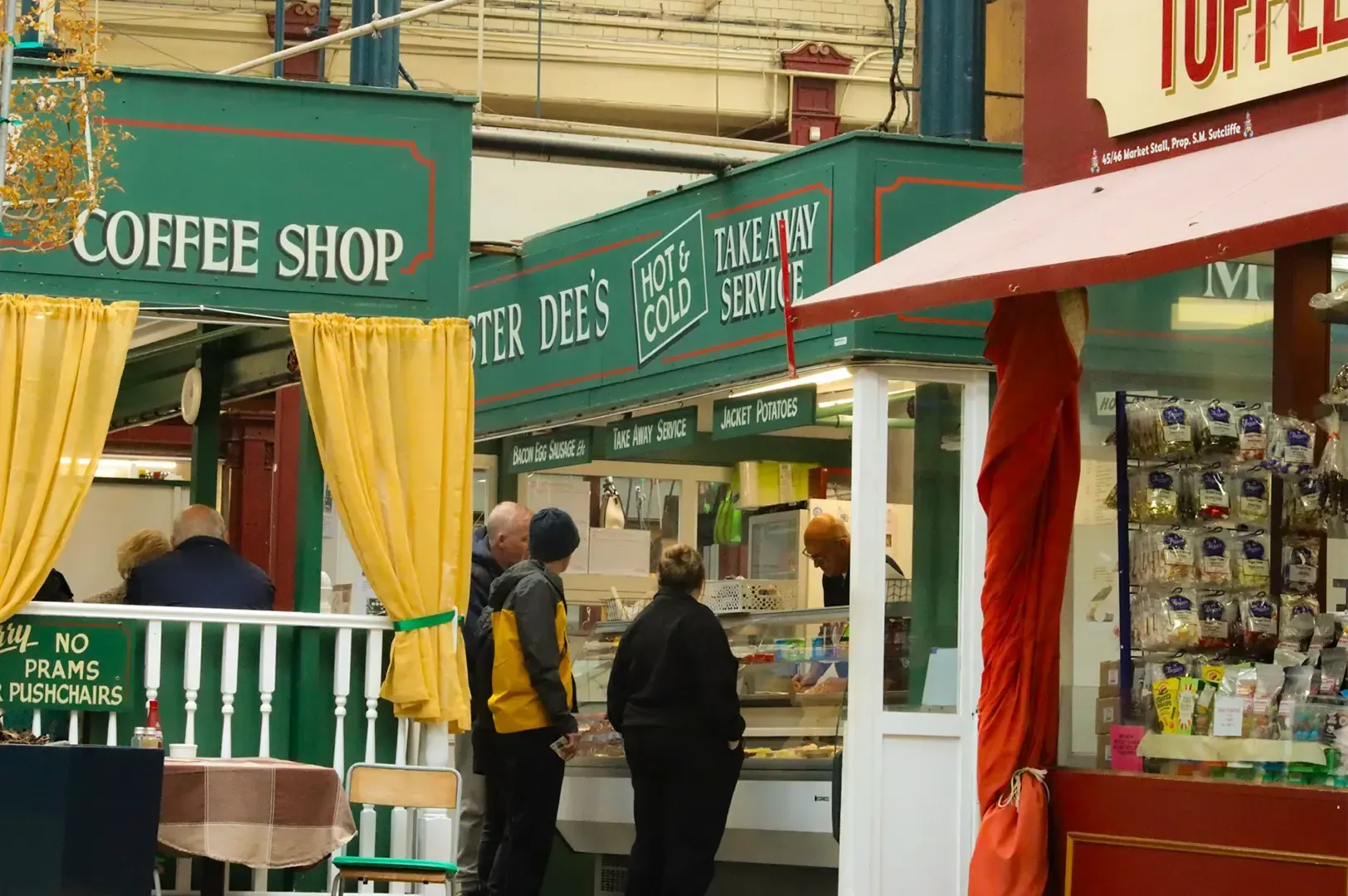 A group of people in front of a coffee shop glass display choosing from the selection, a red stall e
