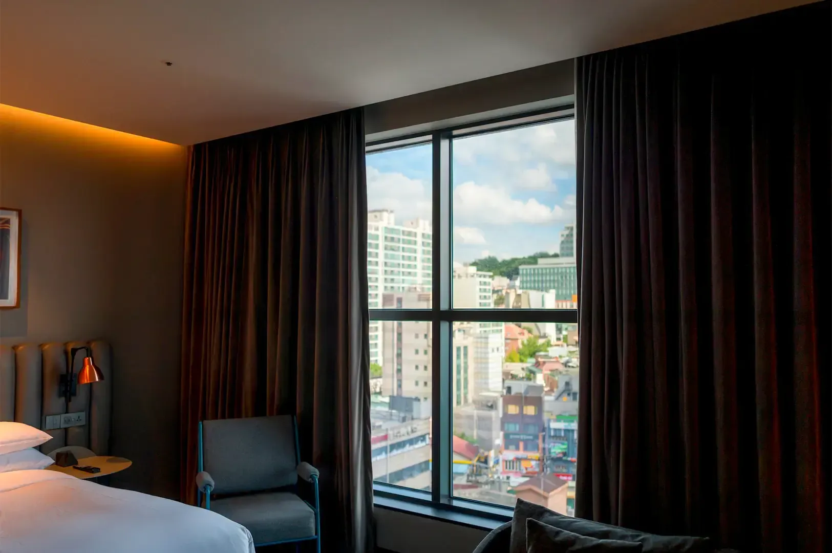 A cozy hotel room interior with parted red curtains revealing a city view outside.