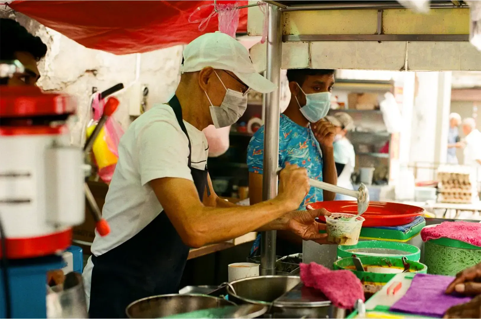A hawker vendor preparing a meal in a container with his ingredients layed out in front.