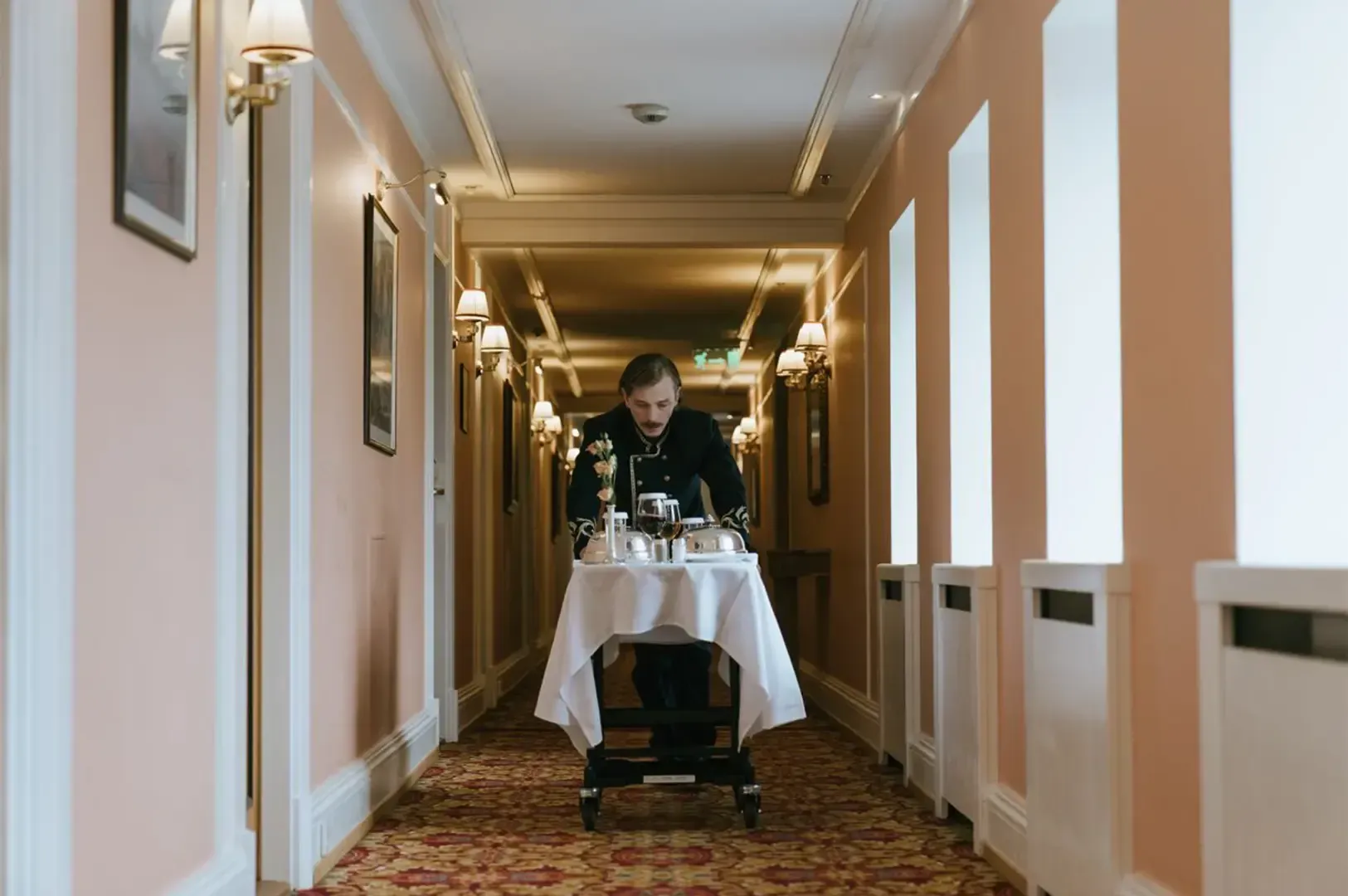 A hotel staff pushing a cart full of dining utensils placed on top of a white cloth, the white and b