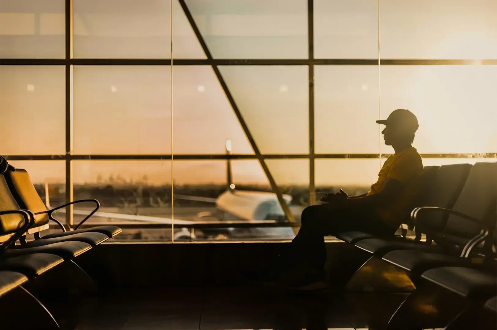 Wide angle shot of a man sitting alone inside an airport beside a huge window with a visible blurred