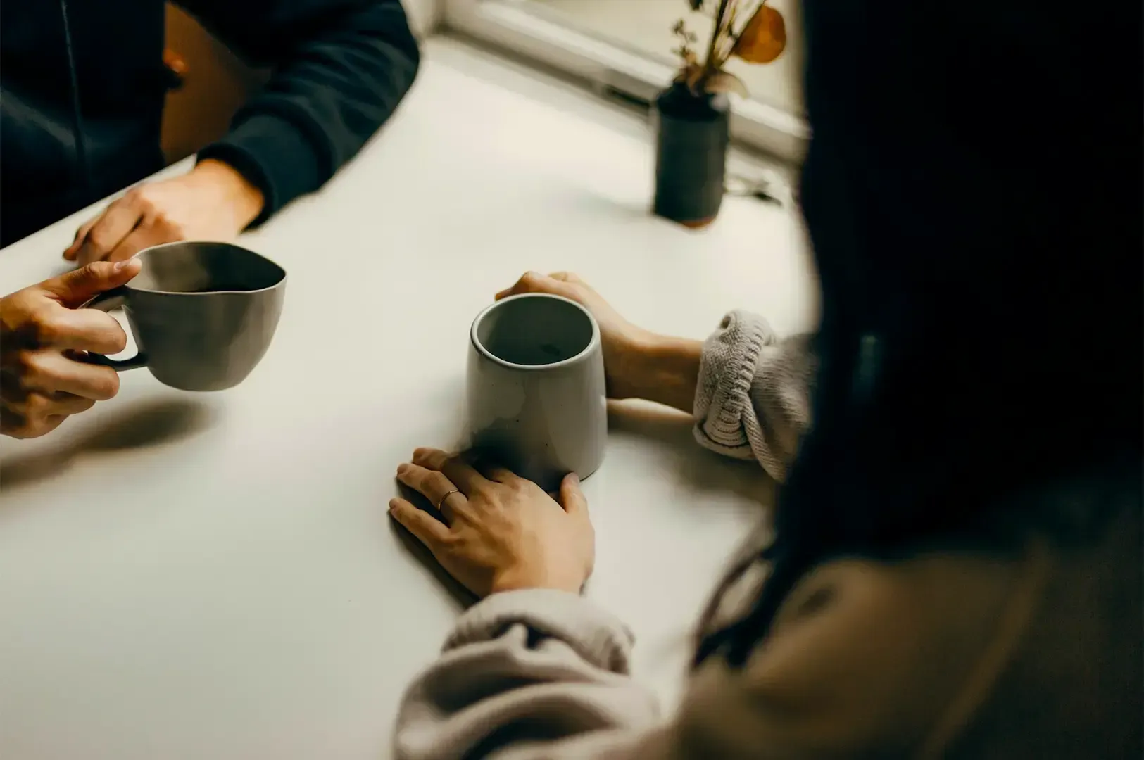 Two people having a conversation over cups of coffee in white mugs.