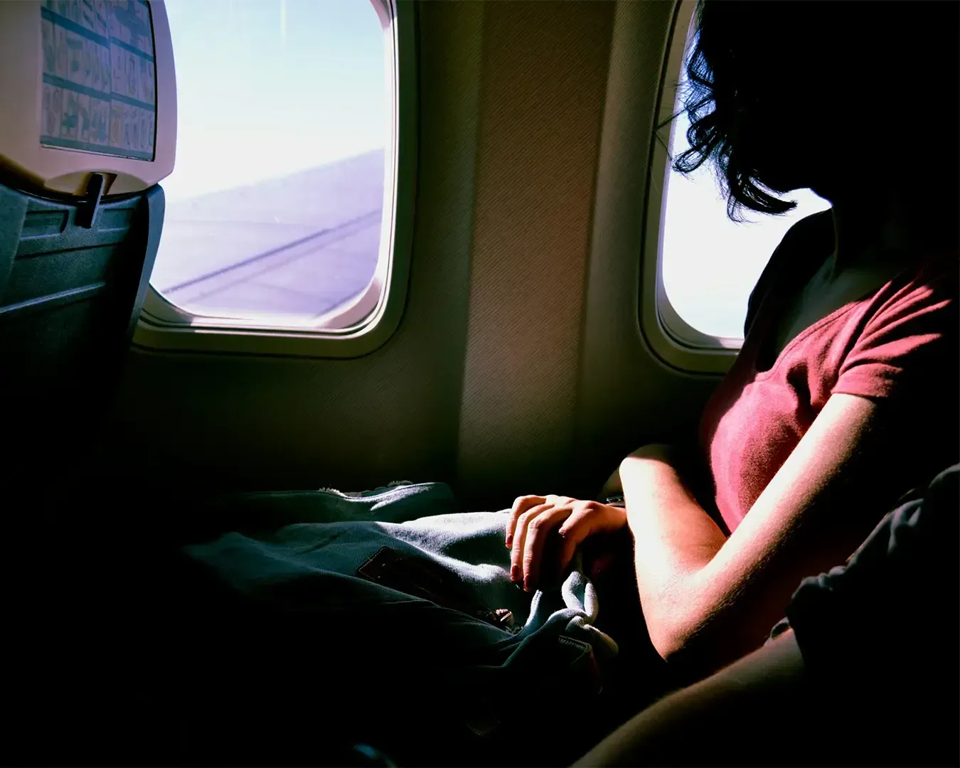 A woman sits beside an airplane window, gazing outside as soft daylight filters through the glass.