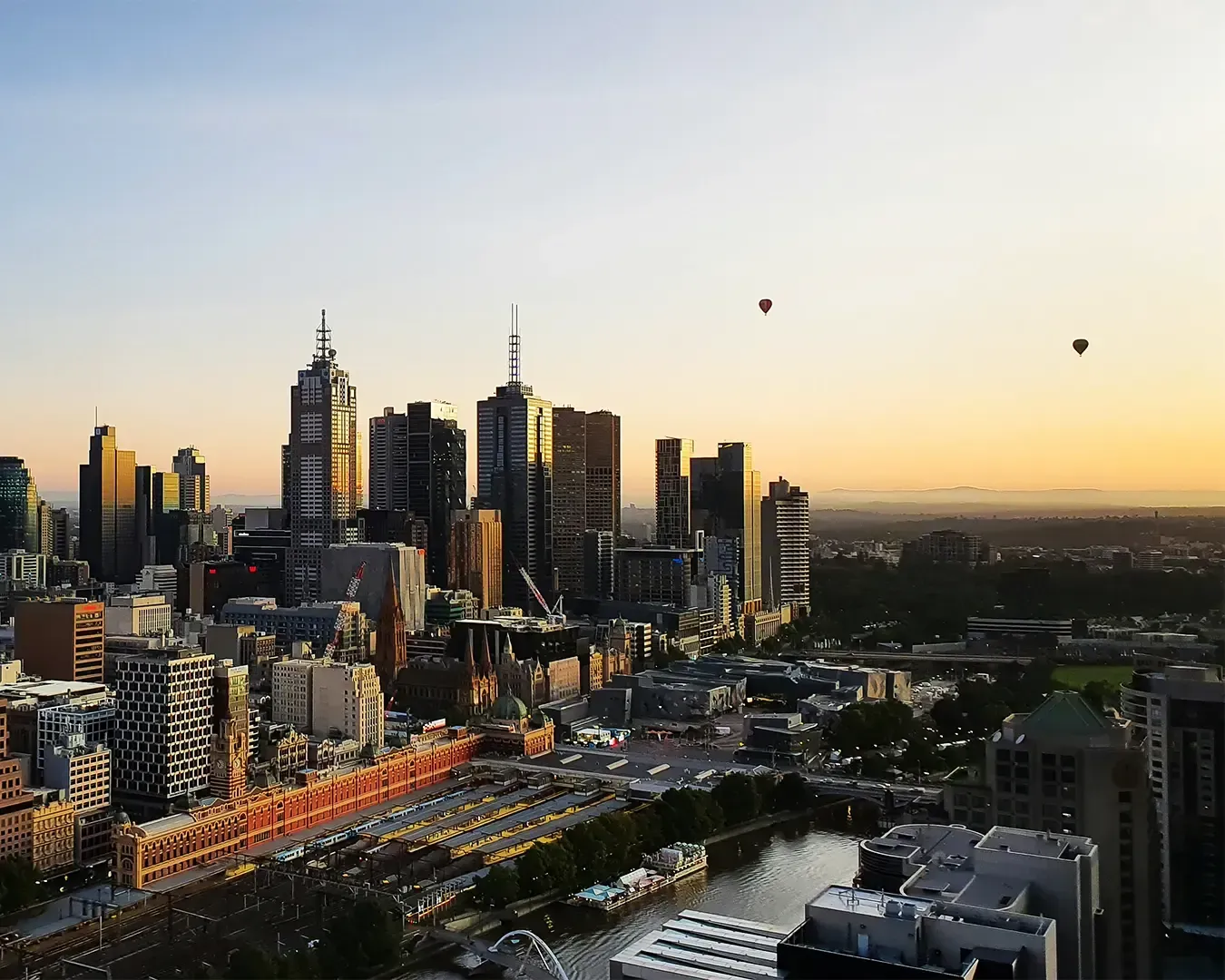 City skyline at sunset with golden light, buildings, and hot air balloons.