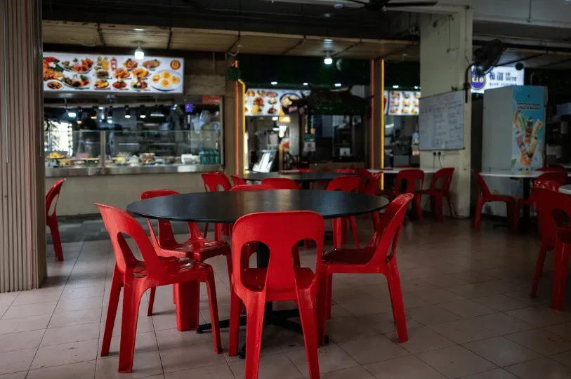 An everyday scene in a traditional Singaporean open-air hawker center or kopitiam. The foreground fe