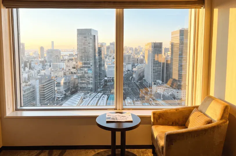 A quiet hotel room interior featuring a yellow armchair and a small round table with a newspaper, lo