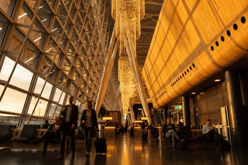 A modern, sunlit airport concourse featuring massive glass windows, curved wood paneling, and striki