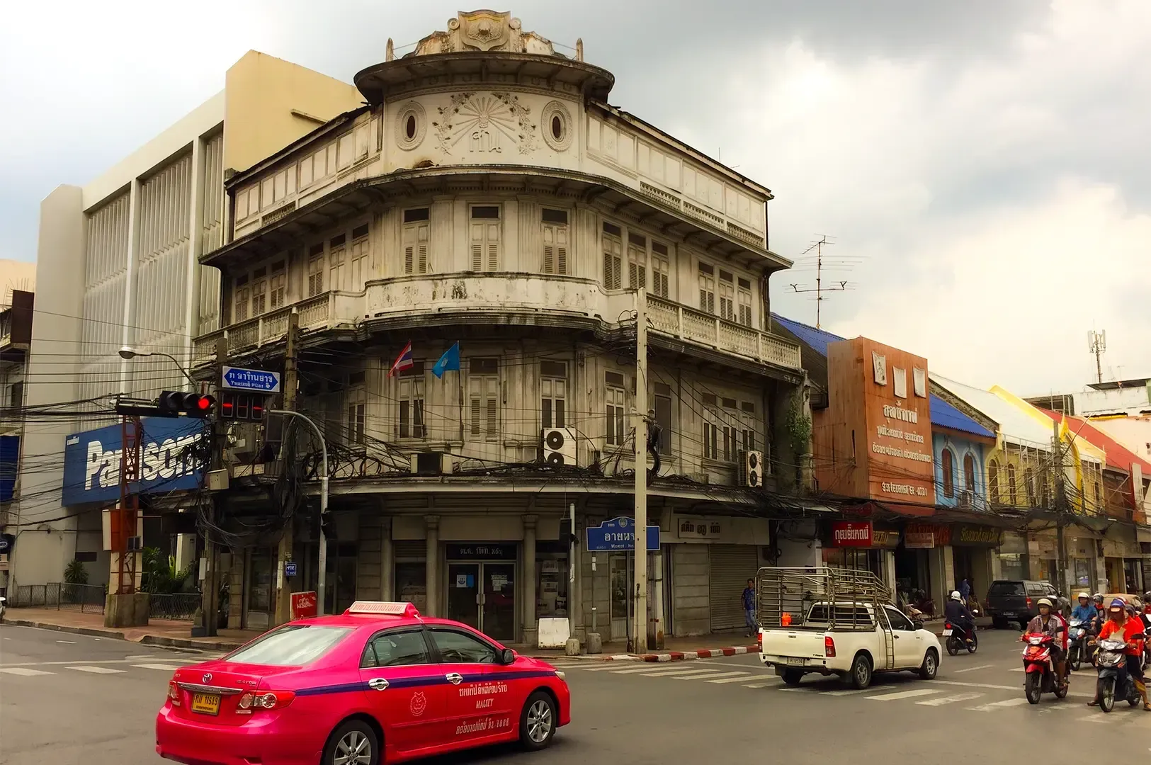 An old building along Charoen Krung street corner with vehicles passing by in front.