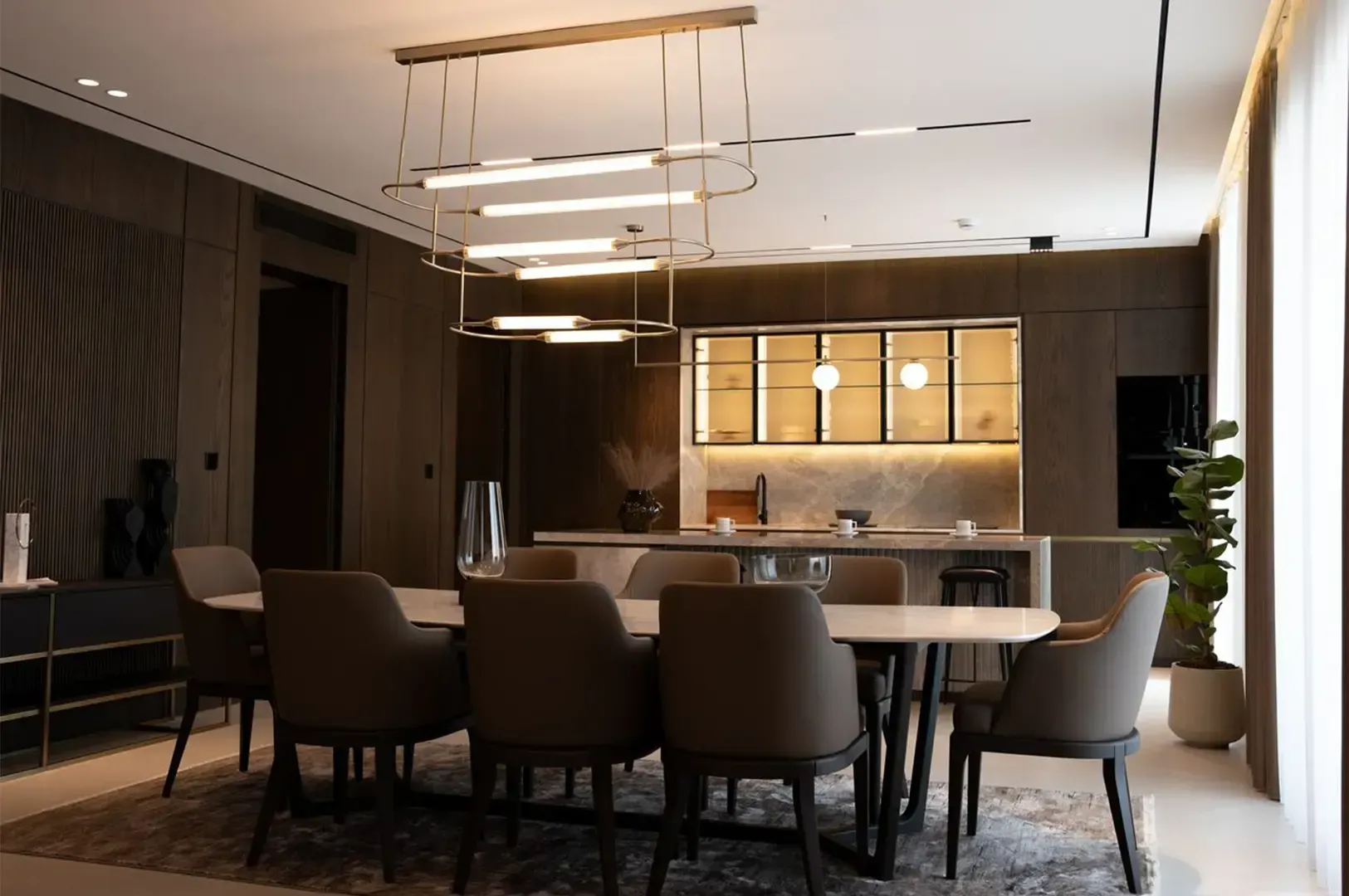 Interior of a house with a table with chairs surrounding it as a centerpiece, a counter with lighted cupboard and an overall brown and white theme in the walls, ceiling, and floor giving a cozy clean vibe.