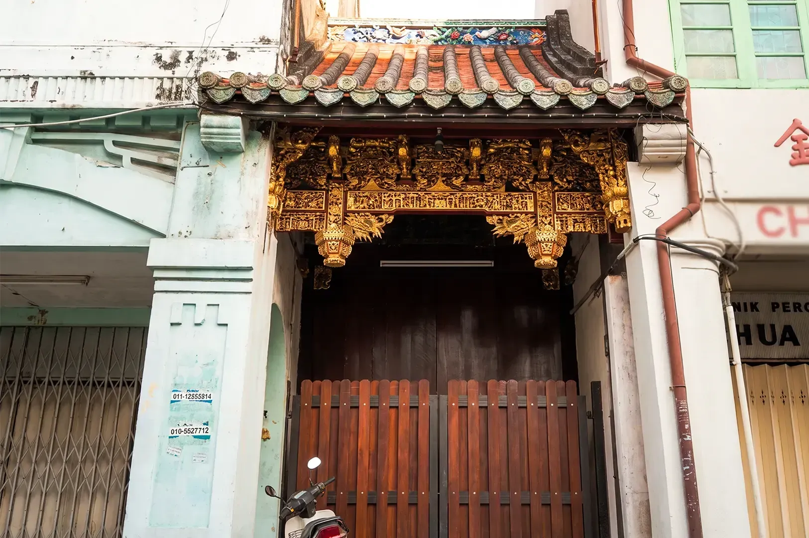 An old Chinese inspired shophouse in George Town, Penang, Malaysia with red tiled roof and gilded designs on the threshold.