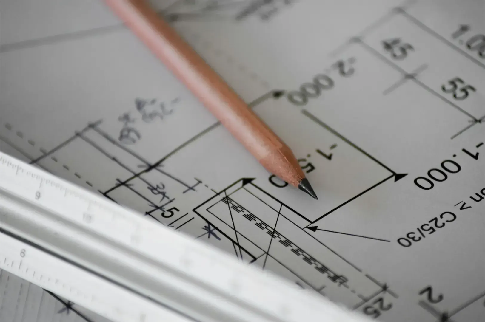 Extreme close up shot of a floor plan on white paper with a pencil and a ruler on top.