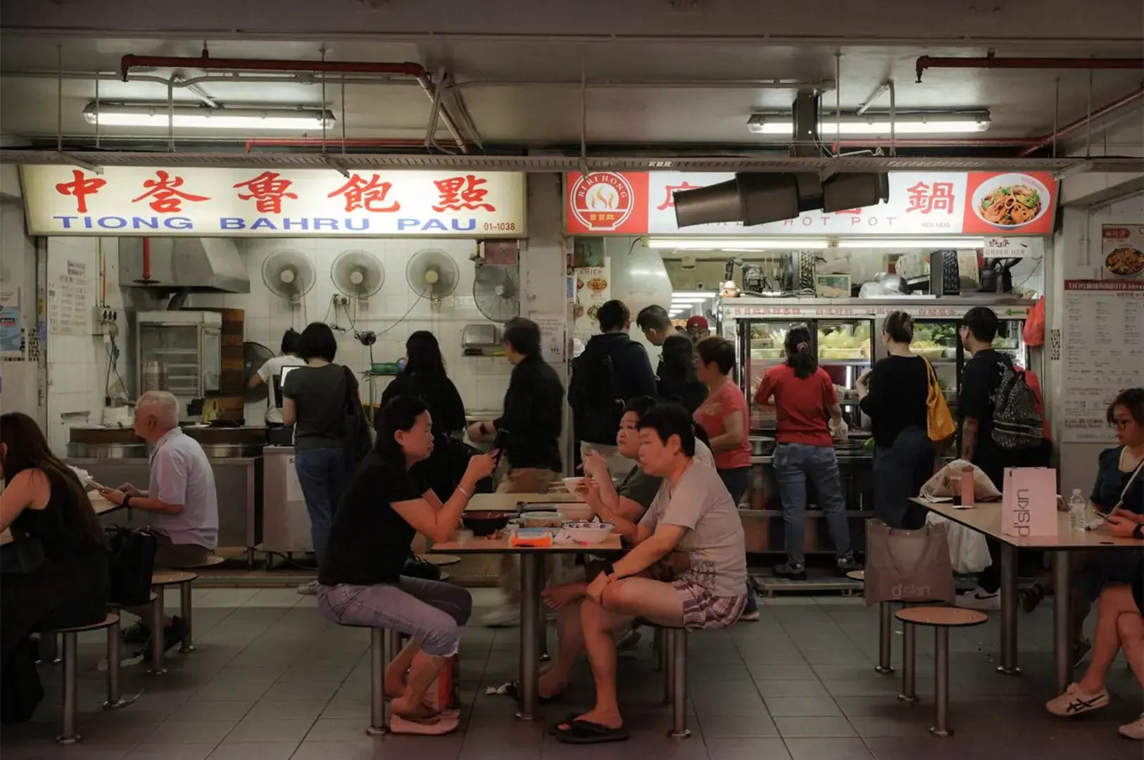 Two hawker stalls side by side each other with customers dining and ordering in front.