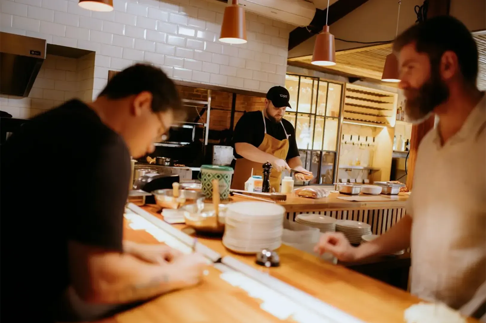 Two people conversing by a chef’s counter as the chef is focused at the background preparing a dish.