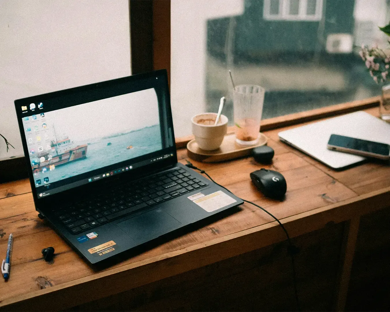 A laptop at a café table, surrounded by the relaxed atmosphere of a coffee shop. The setting reflects a casual work environment, with the laptop open and the person focused on completing tasks while enjoying the café ambience.