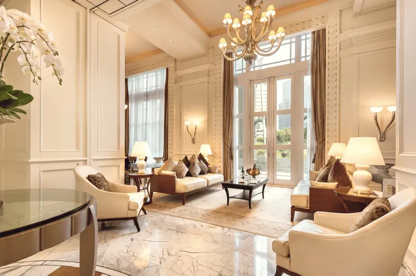 An opulent, high-ceilinged living area uses a central rug and symmetrical sofa placement to define a cohesive conversational space. Tall glass doors draw the eye outward, highlighting how vertical space and light make the room feel grand yet purposeful.