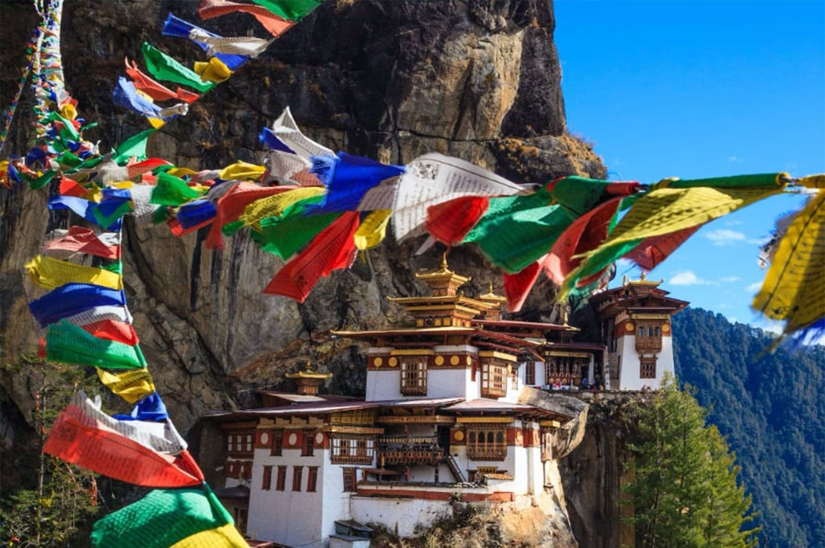 The iconic Paro Taktsang, also known as Tiger's Nest Monastery, perched precariously on a cliffside in Bhutan, framed by colorful Buddhist prayer flags blowing in the wind.
