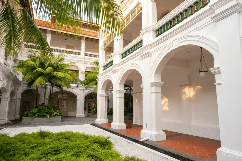 An inviting arched outdoor corridor of a classic luxury hotel, featuring terracotta floors and lush tropical greenery that evoke a sense of a serene, private retreat.