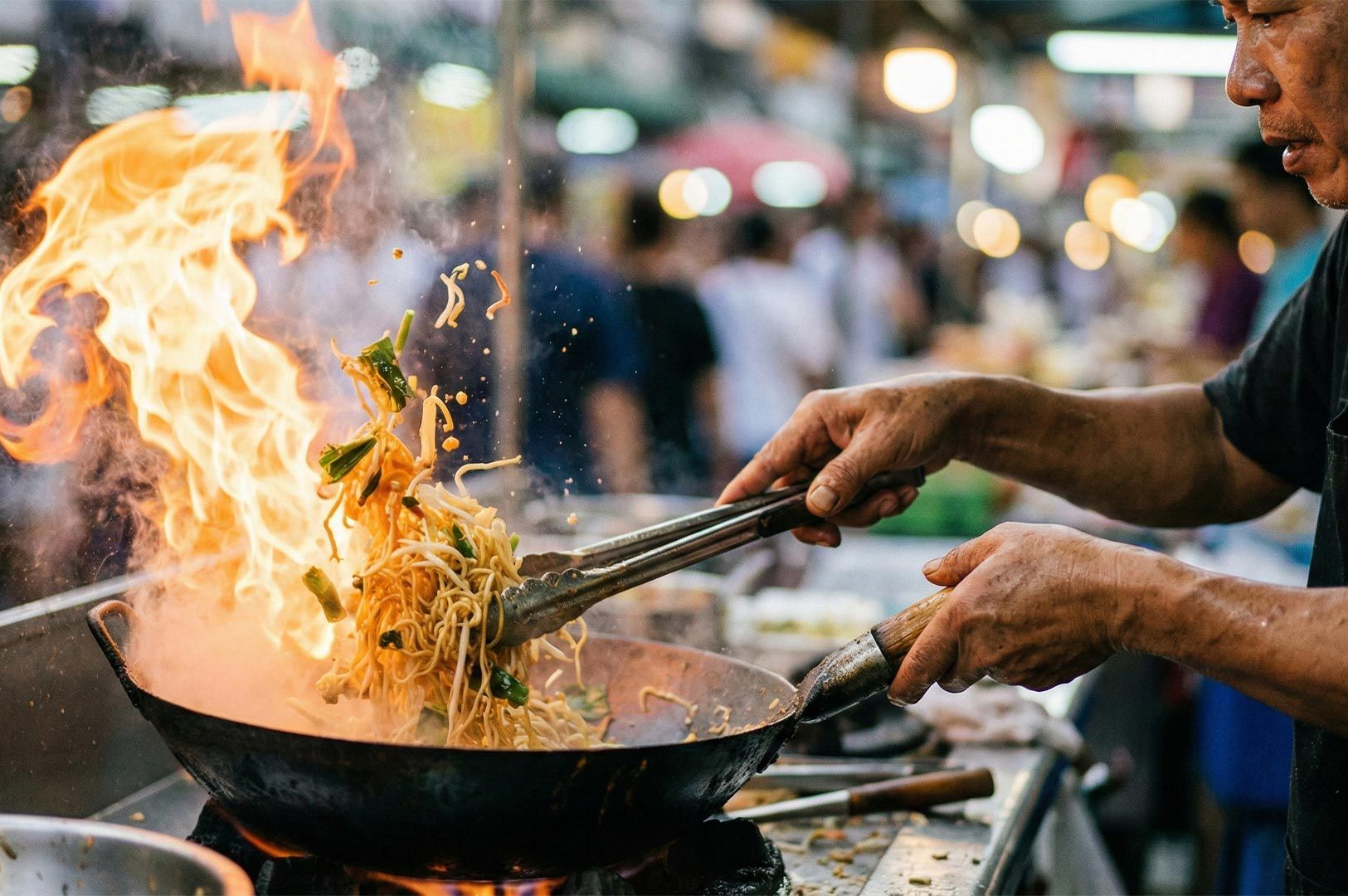 Close-up action shot of a street food chef stir-frying noodles in a wok, creating a large burst of fire and flames known as wok hei.