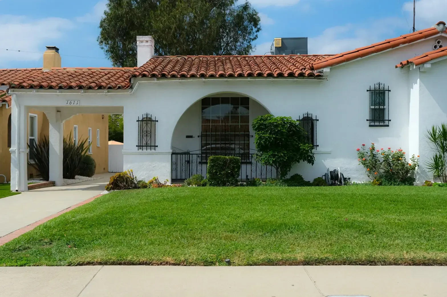 A residential front lawn with the left half of the white building visible revealing a walkway that connects with the street in front.