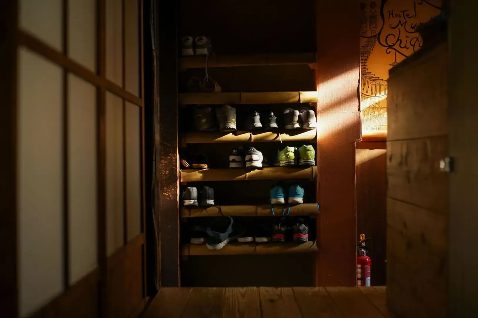 A number of shoes placed in a wooden shelf before a threshold with a traditional Japanese architecture.