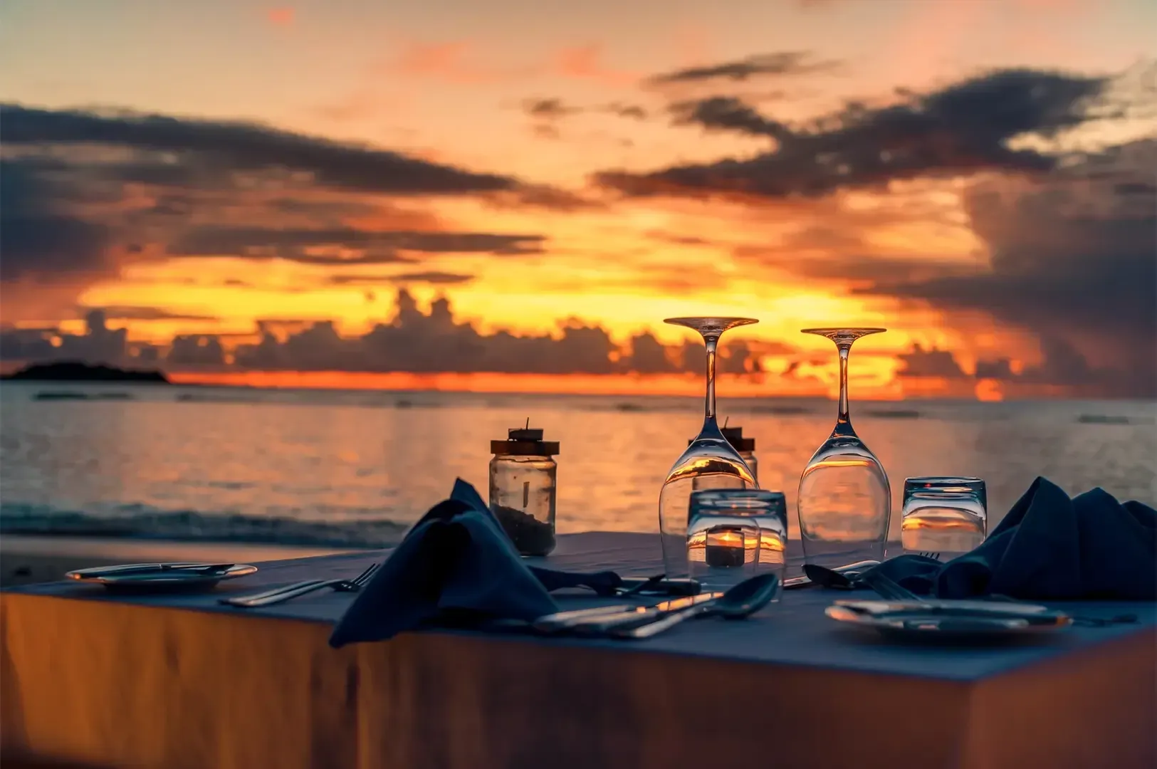 A fine dining table with upside down glasses and neatly arranged cutlery with a setting sun in the background casting a golden light.