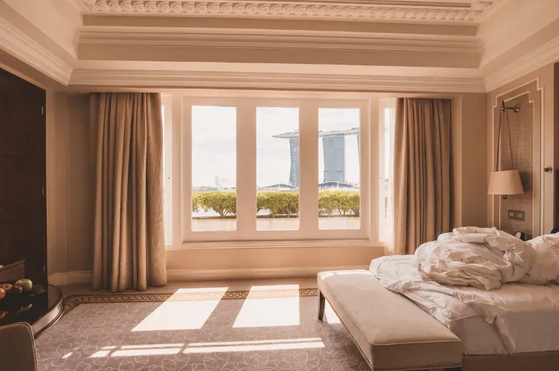 A partially unmade bed sits to the right of a large bay window framing a spectacular daytime view of the Marina Bay Sands. The open floor space between the bed and window highlights how unobstructed sightlines can dramatically expand the feel of a room.