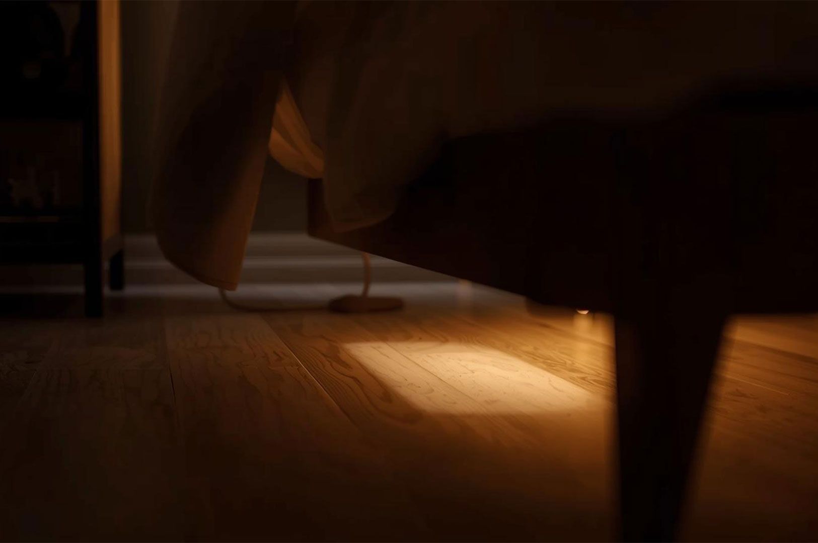 Soft, warm ambient lighting illuminating the wooden floor from underneath a bed frame, functioning as a night light.