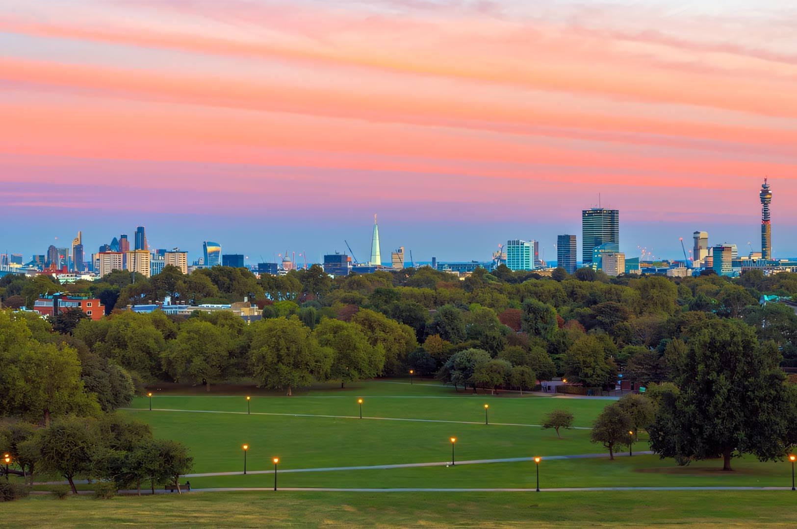 A panoramic view of the London skyline at sunset from Primrose Hill, featuring the Shard and BT Tower.