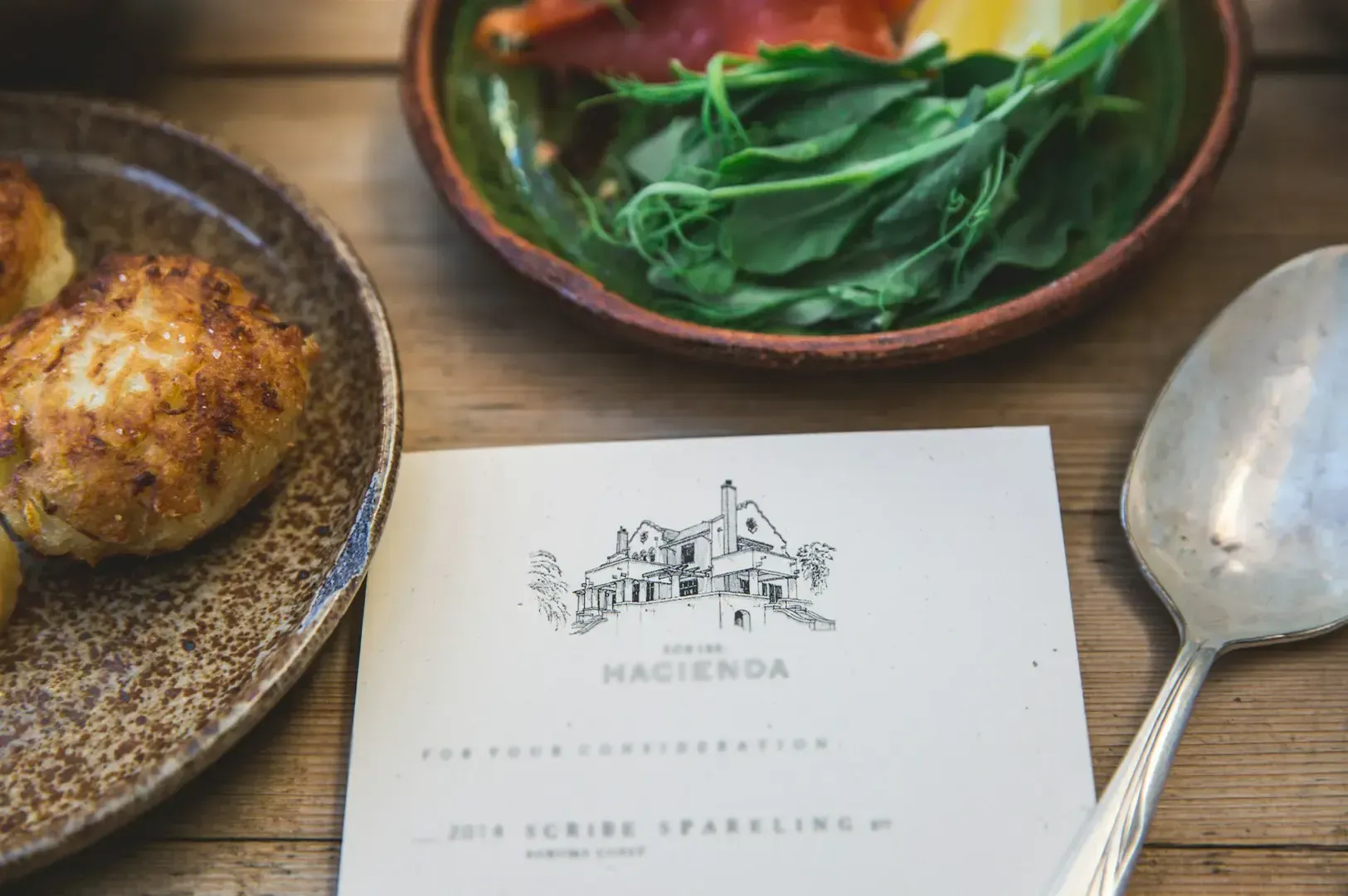 A minimalist designed menu with dishes served in textured bowls arranged on top of a wooden table.