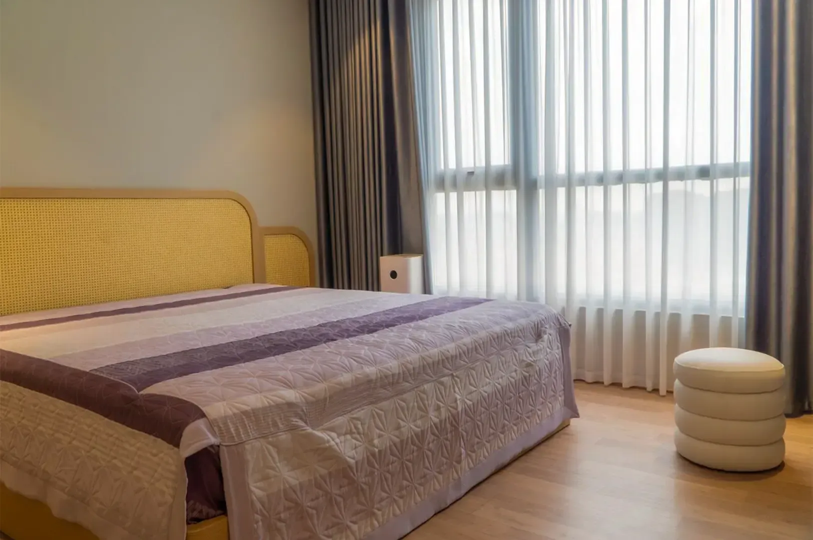 A hotel bed beside a wide window, a thin curtain letting through soft white sunlight.