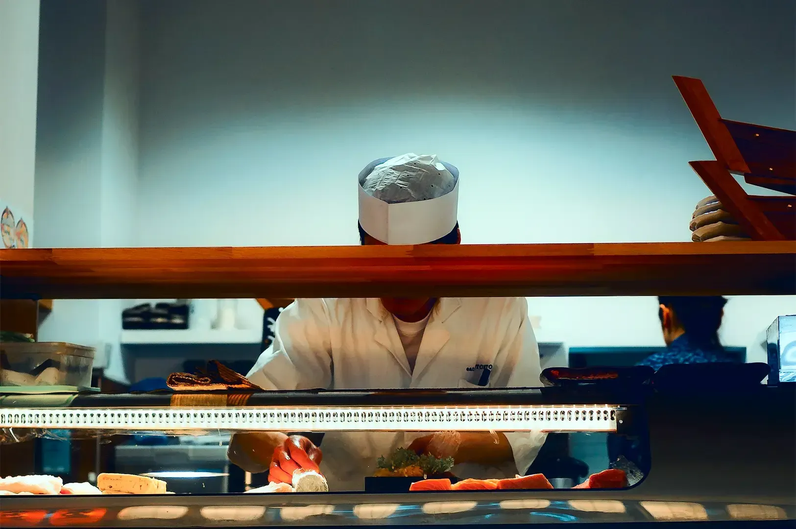 A chef behind a counter working with fresh ingredients displayed in front.