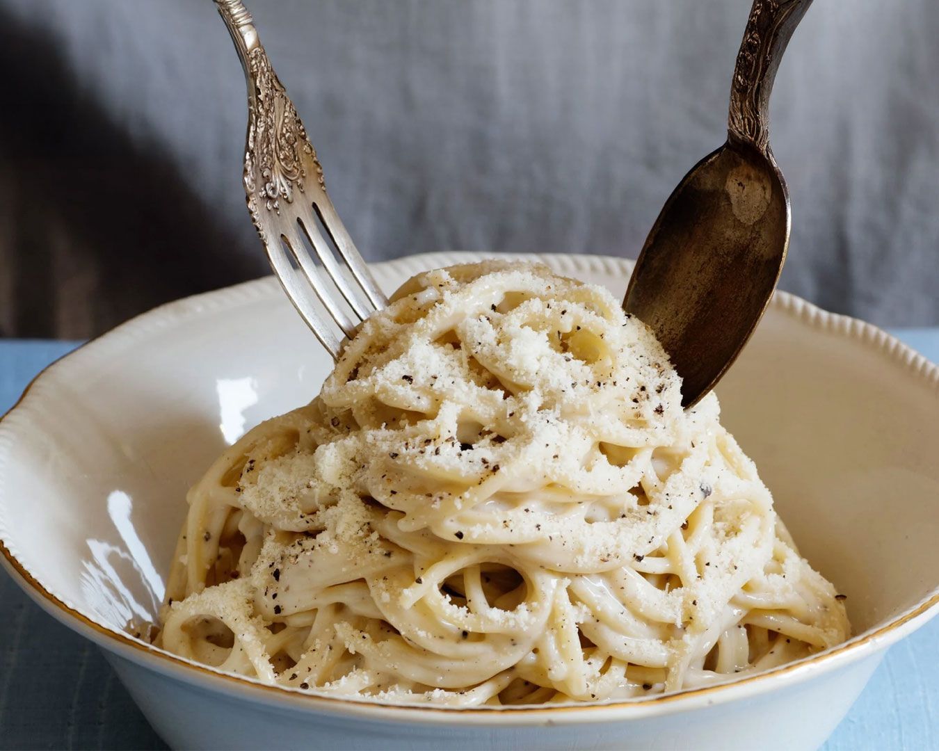 A close-up of a plate of cacio e pepe pasta coated in creamy cheese sauce and topped with cracked black pepper, served on a simple ceramic dish.