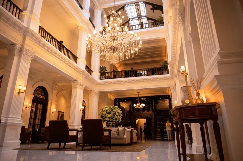 A grand luxury hotel lobby featuring an aroma diffuser and reed sticks on an elegant wooden table in the foreground, highlighting the subtle use of scent to welcome guests.