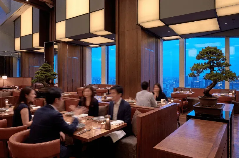 An upscale Japanese restaurant at twilight, featuring warm wood paneling, decorative bonsai trees, illuminated geometric ceiling fixtures, and diners enjoying their meal in cozy booths overlooking a panoramic city skyline.