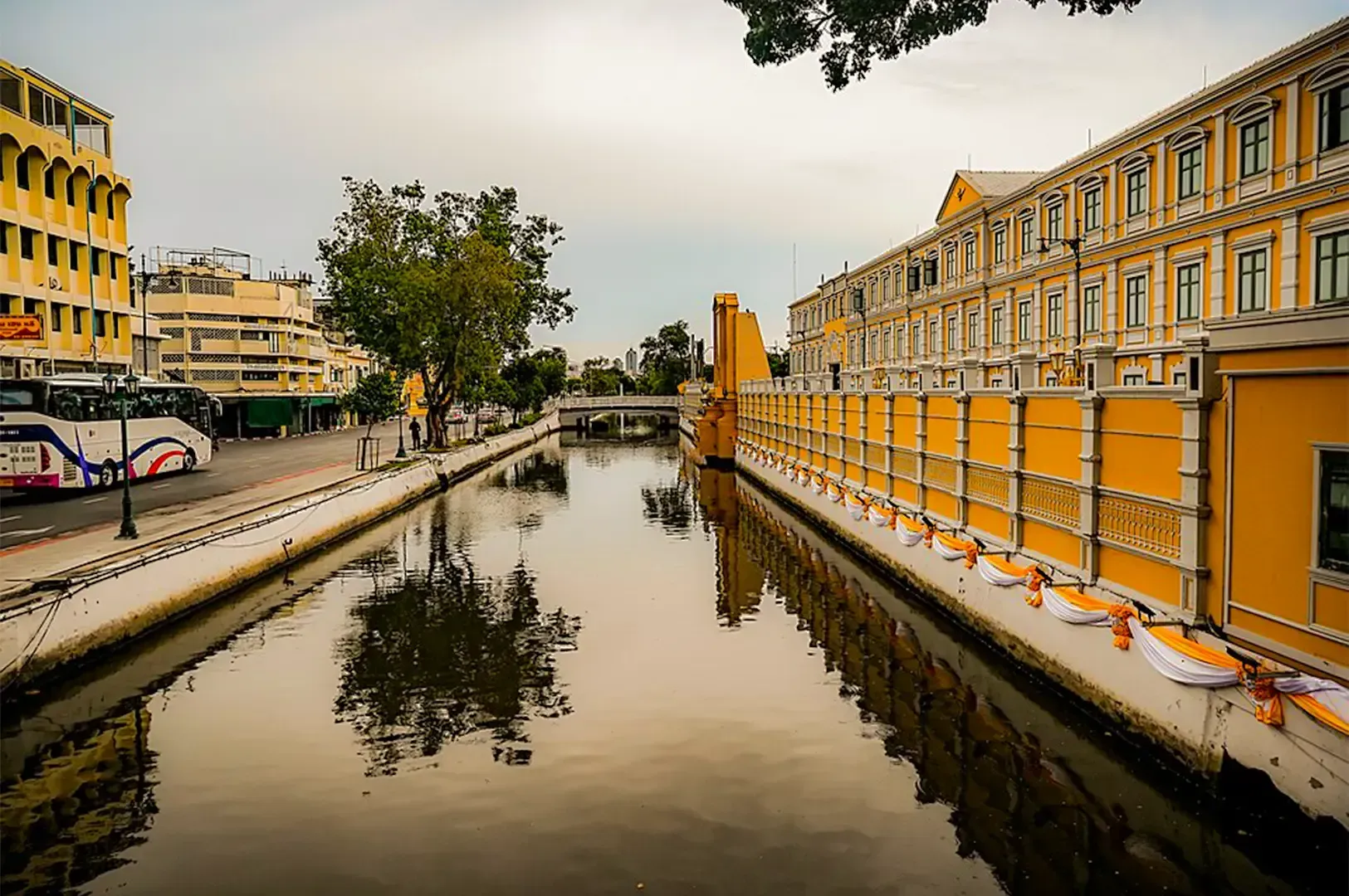 Thonburi Canal with a line of bright colored buildings on the right and a road on the left.