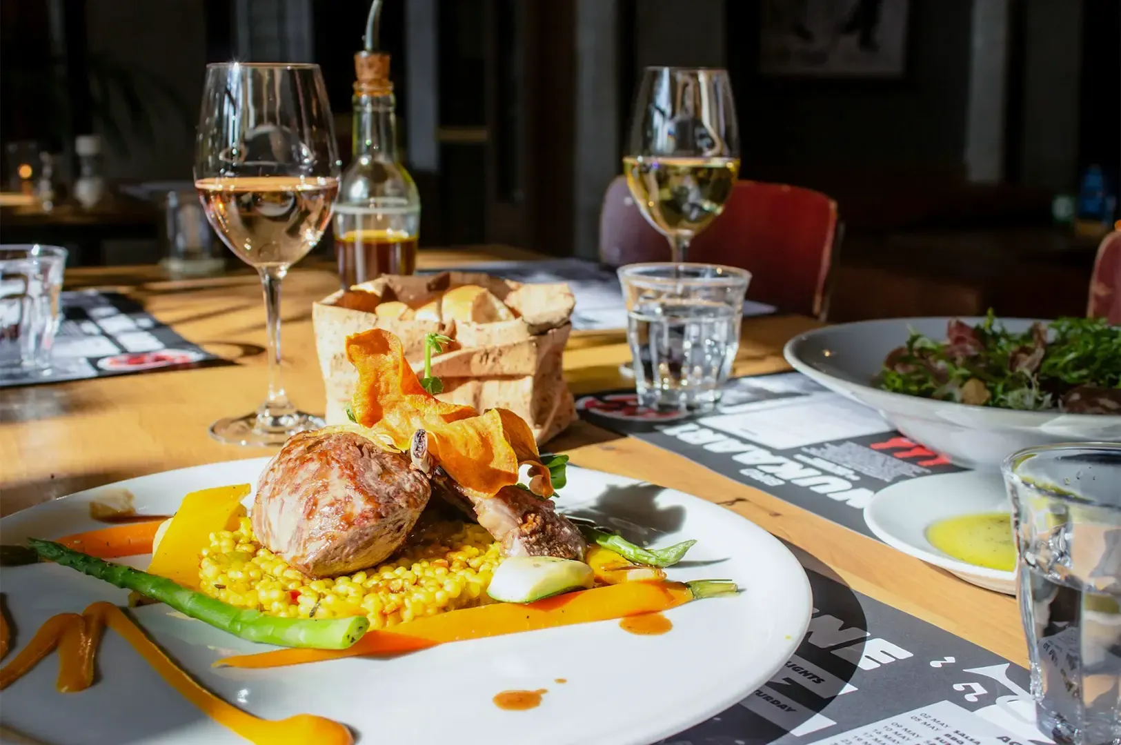 A meat and veggies dish plated on a white platter arrange on top of a table with glasses and other dishes.