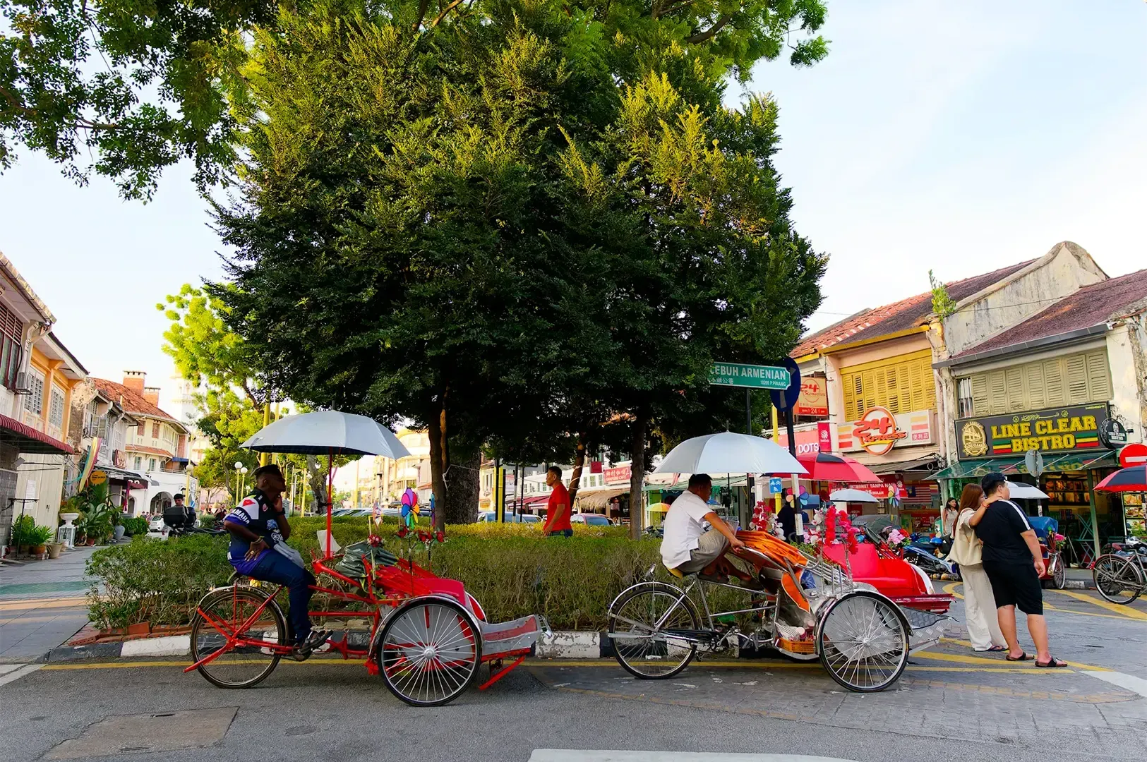 George Town, Penang with people riding red vehicles along the street with shophouses lined up on either side.
