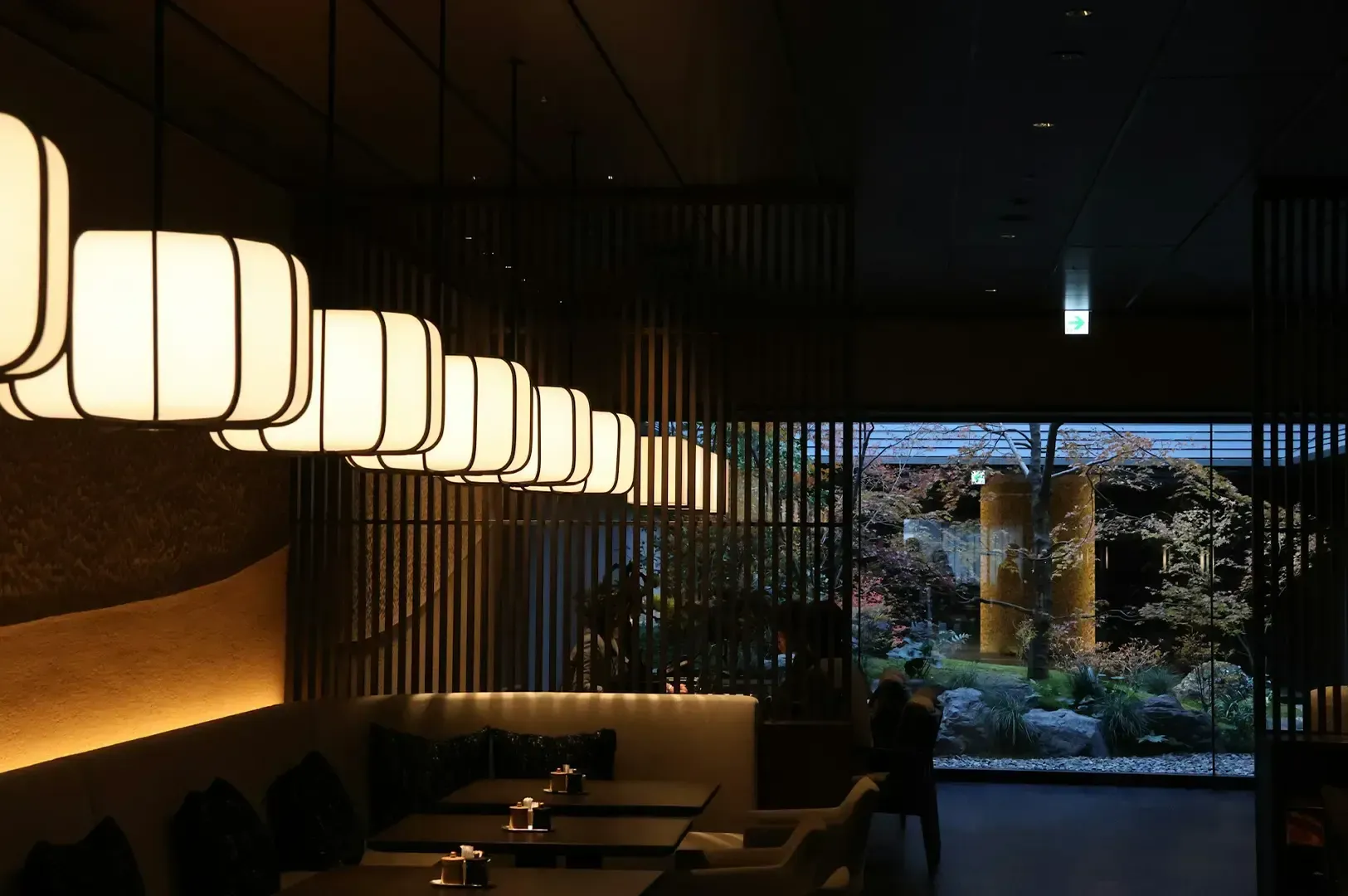 A dim and warmly lit Japanese establishment with an open entrance and empty seats and tables visible, giving a calm and slow ambience.