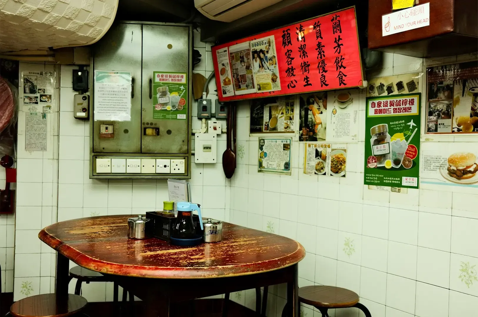 An empty wooden dining table with posters and menu items graphics displayed on the right against a white tile wall.