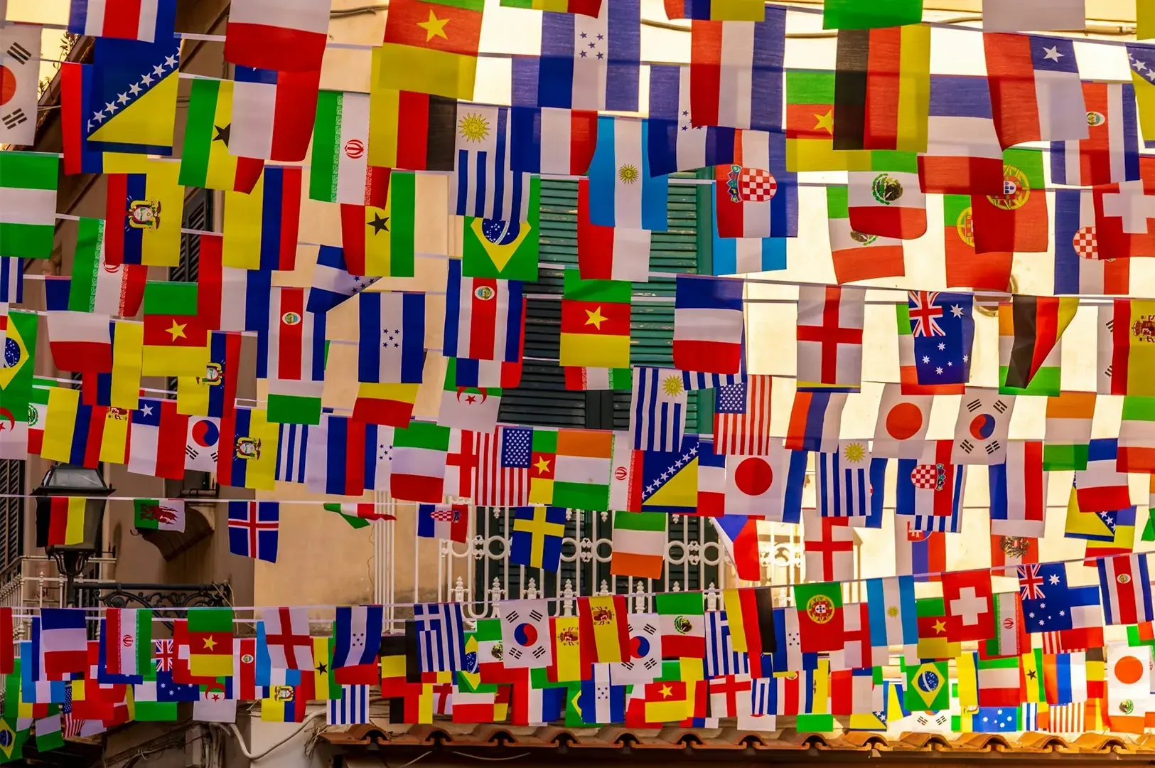 A variety of country flags hung on different lines in front of a light yellow painted building.