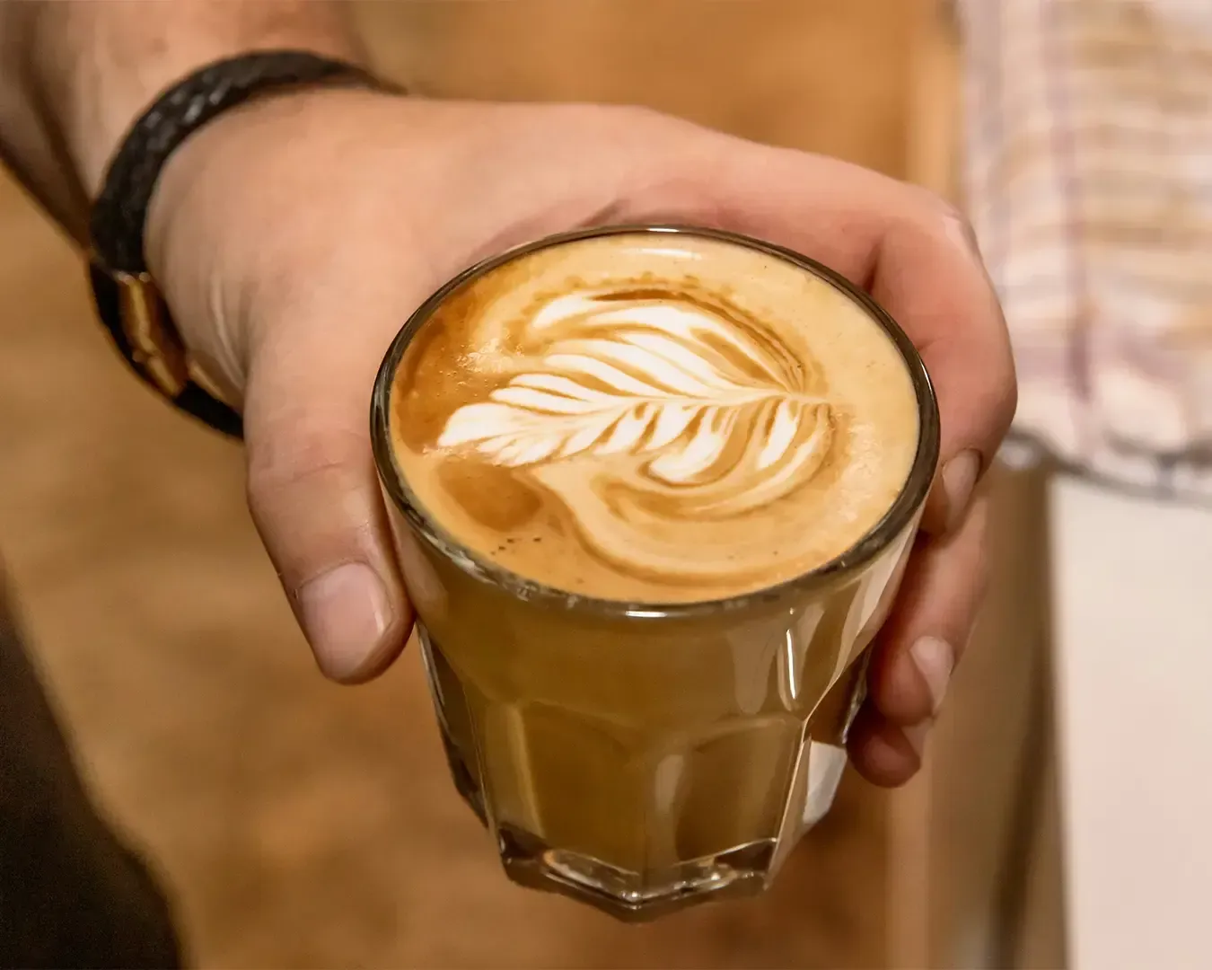 A hand gently holding a cup of freshly made coffee with beautiful latte art, highlighting the smooth foam and rich espresso beneath.
